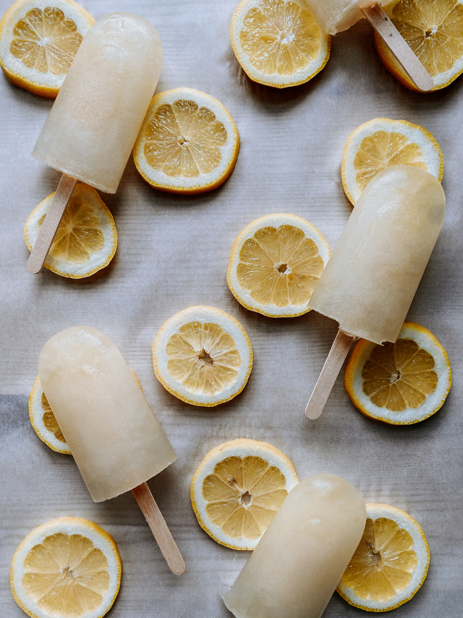 lemon ice pops and lemon slices resting on a parchment lined tray