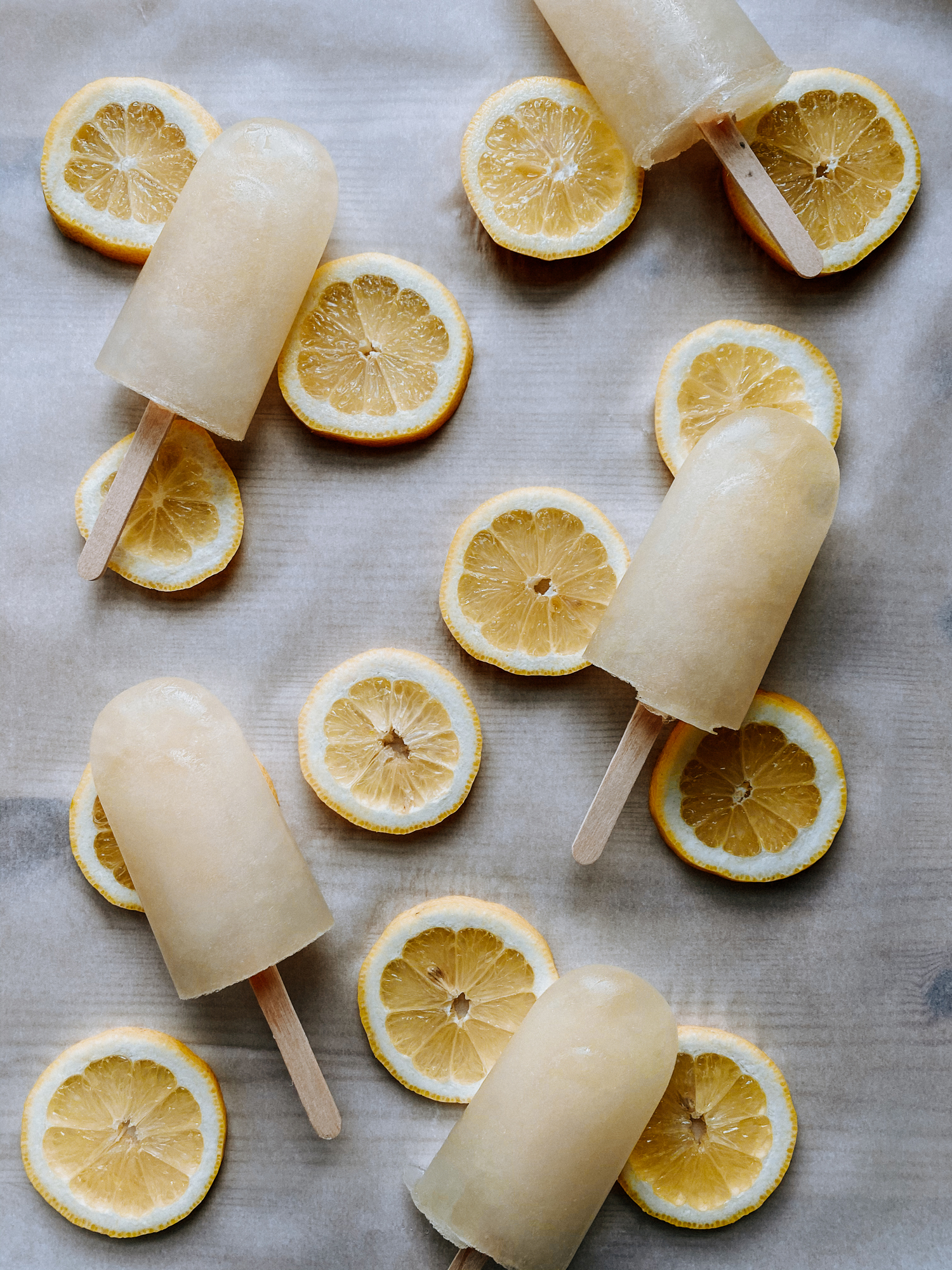 Lemon Ice pops laying on slices of lemon on a tray