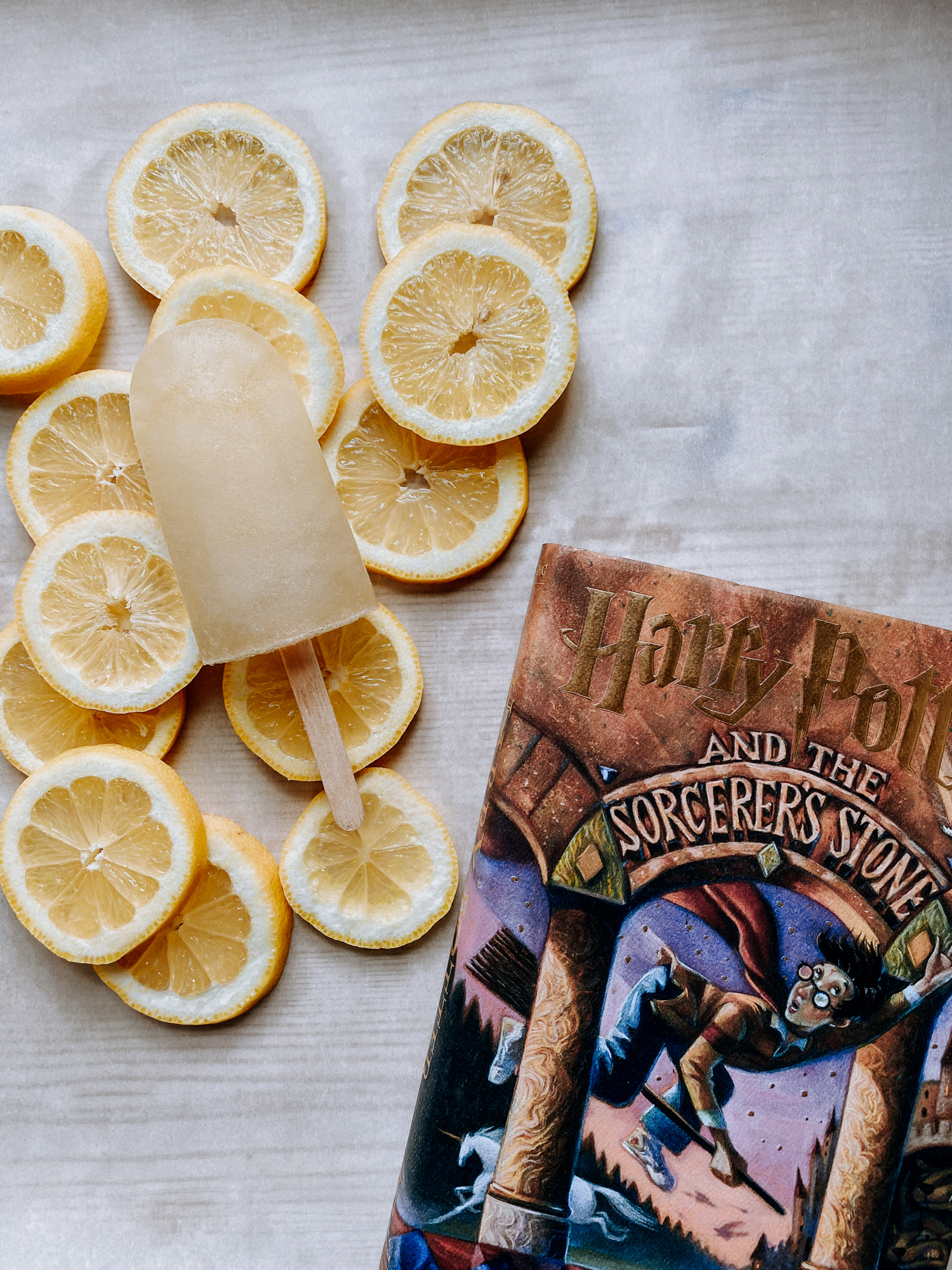 a white surface with lemon slices, a lemon ice pop, and a harry potter book resting on top