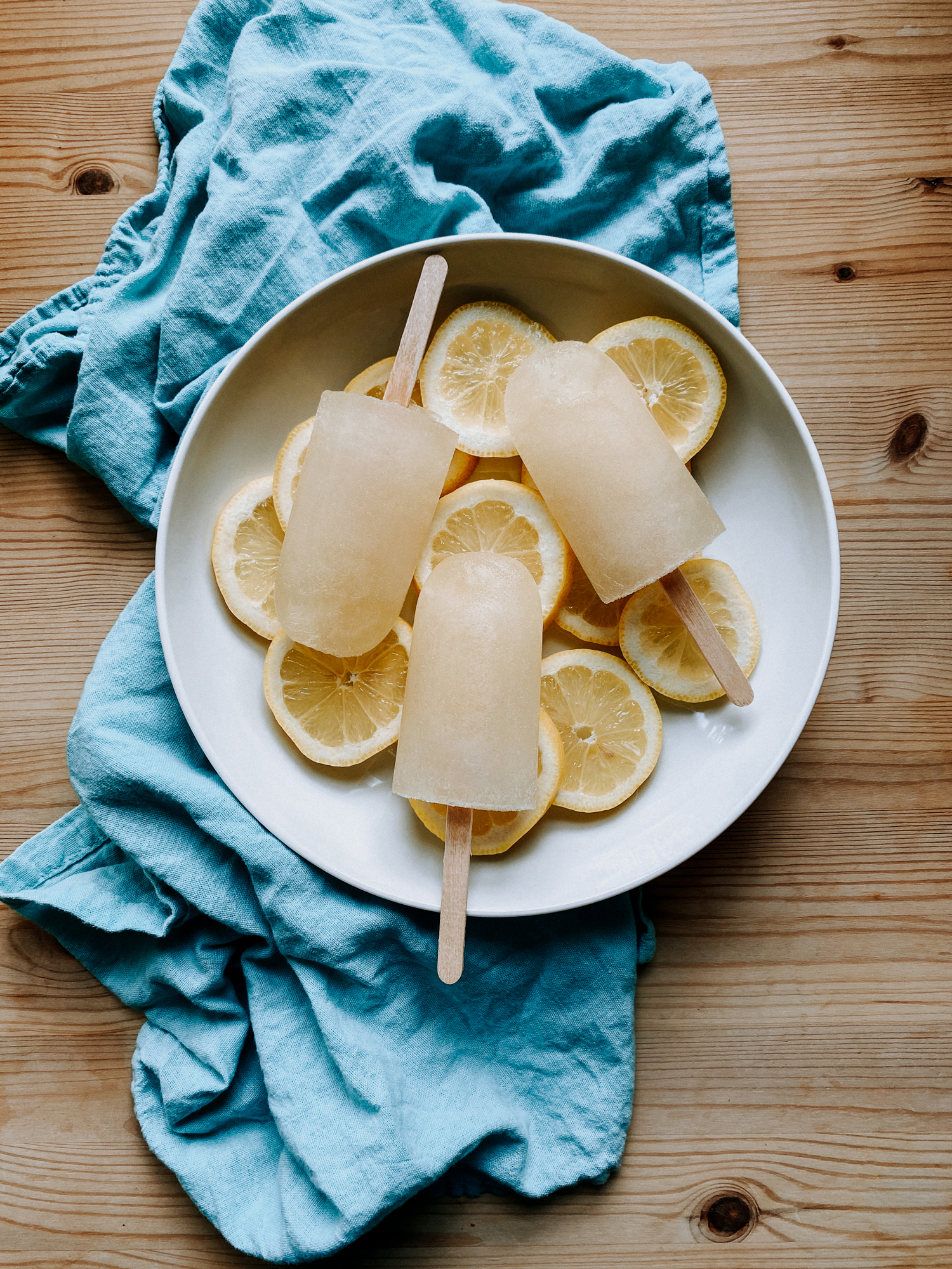 a white bowl filled with lemon slices and lemon popsicles on a blue towel on top of a wooden table