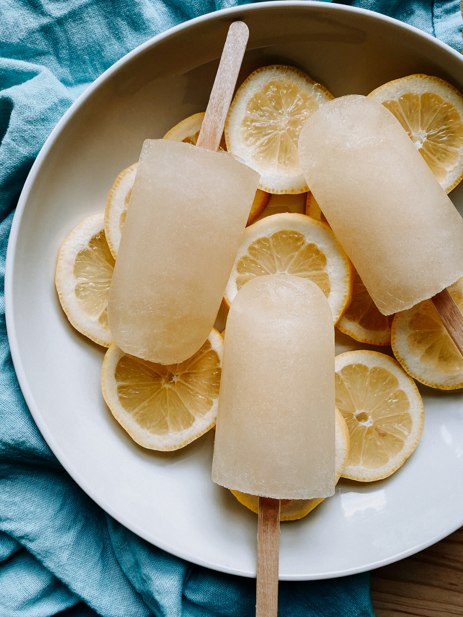 lemon popsicles and lemon slices in a white bowl resting on a blue towel