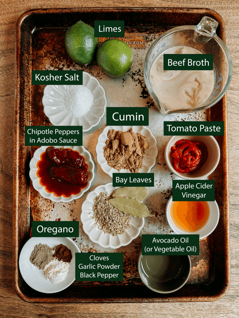 Tray filled with labeled ingredients for Instant Pot barbacoa beef, including limes, chipotle peppers in adobo sauce, cumin, oregano, tomato paste, and spices.