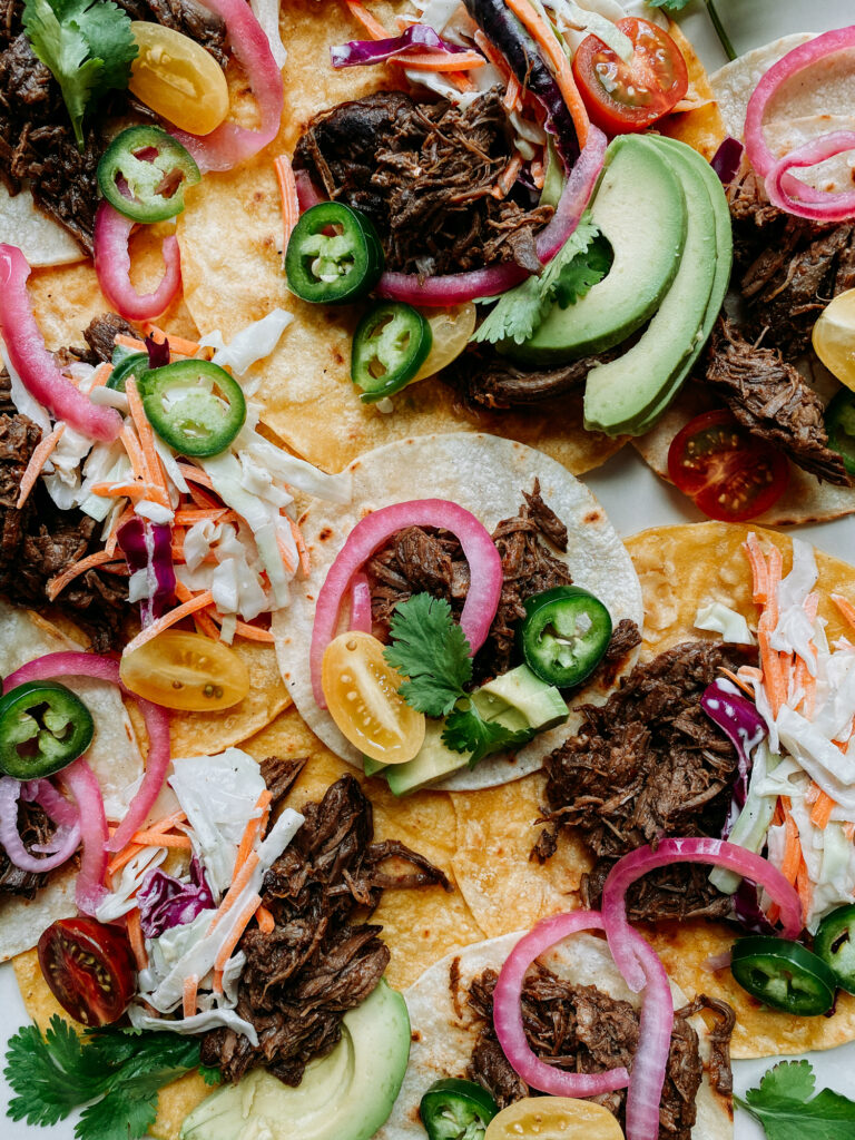 Taco platter with shredded barbacoa beef and fresh toppings like avocado, cilantro, and slaw.