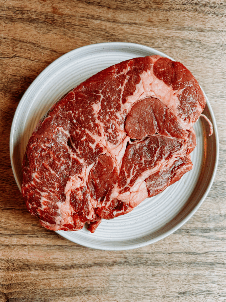 Uncooked beef chuck roast on a plate, showing rich marbling—ideal for making tender, shredded barbacoa beef.