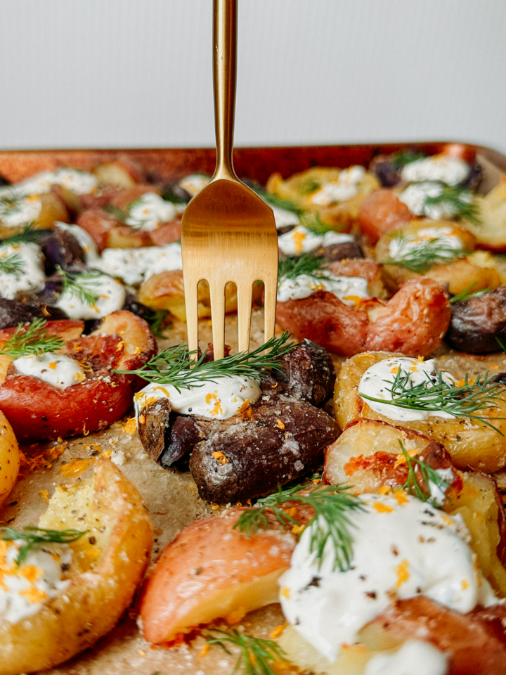 a gold fork piercing into a smashed potato with dill and cream sauce
