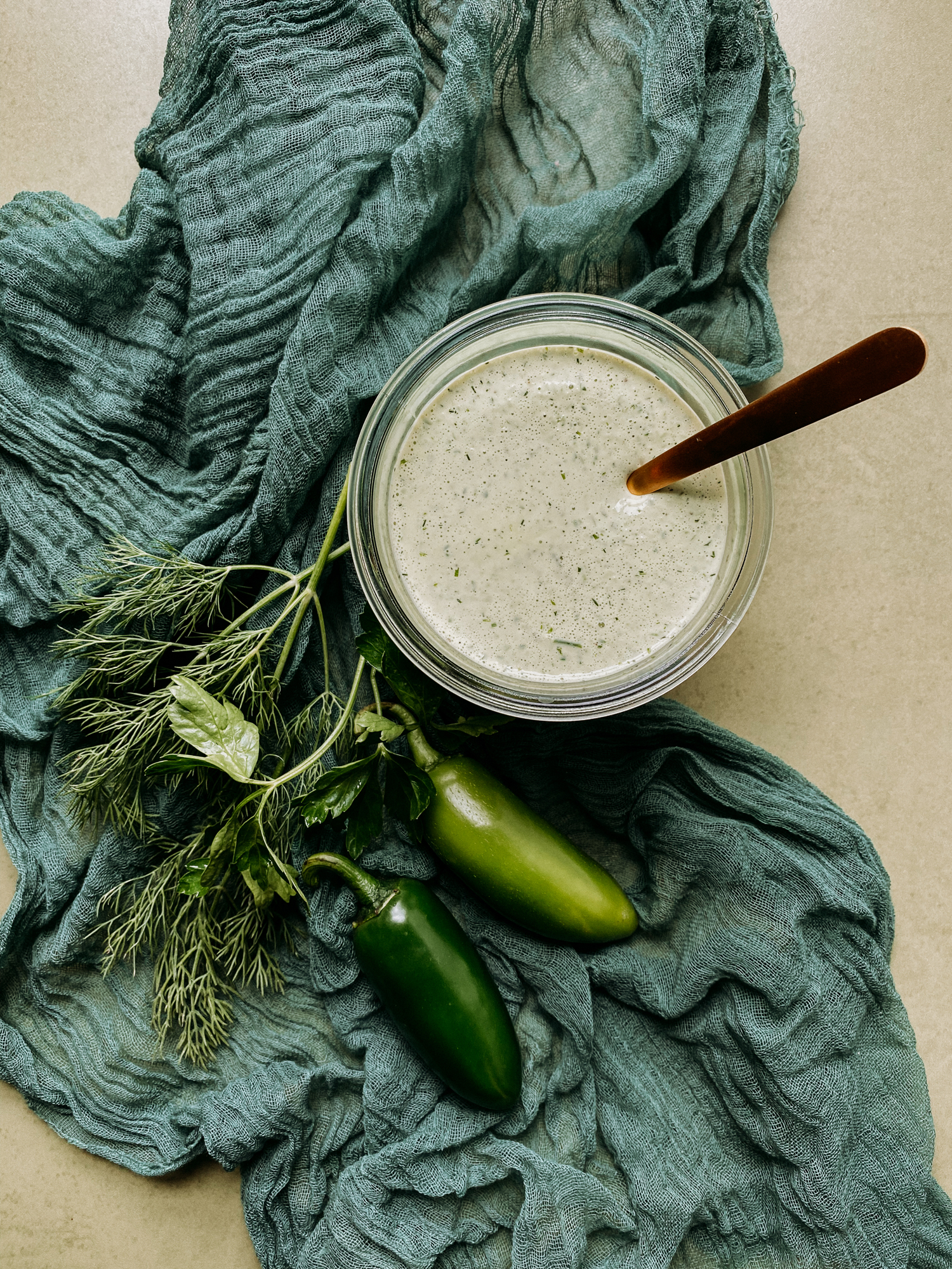 Buttermilk Jalapeno Ranch Dressing in a glass jar with a gold spoon resting in the jar and everything resting on a green cloth