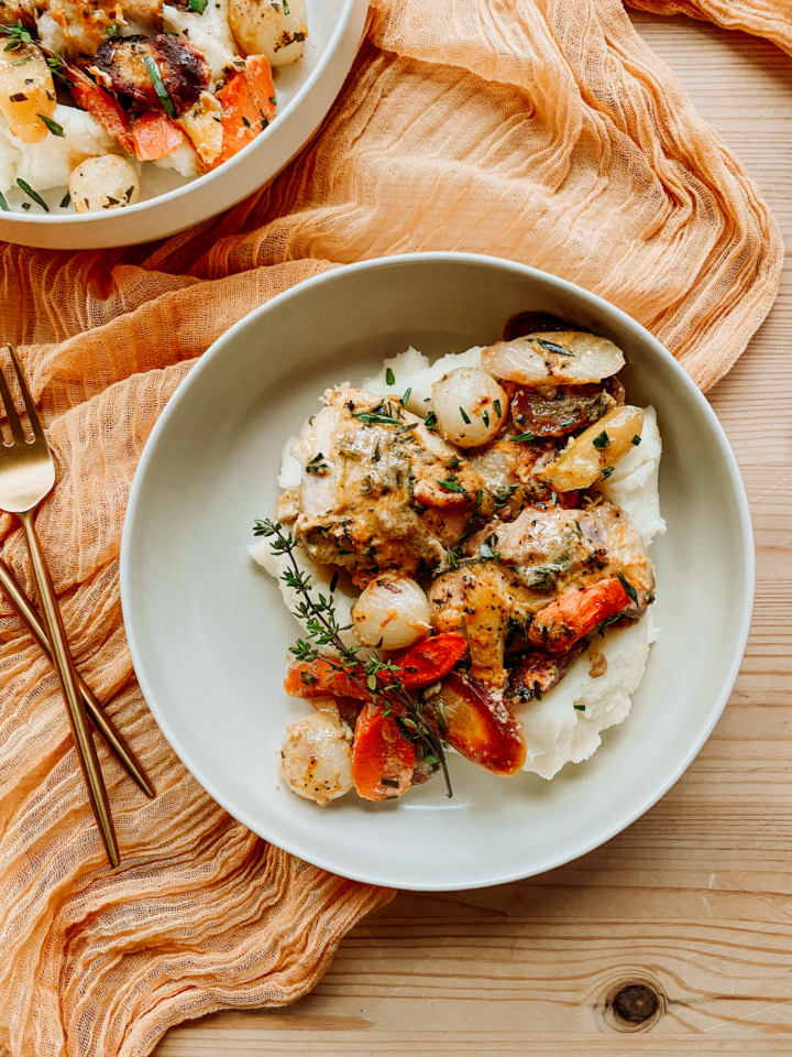 a white plate with chicken thighs in orange dijon cream sauce and mashed potatoes