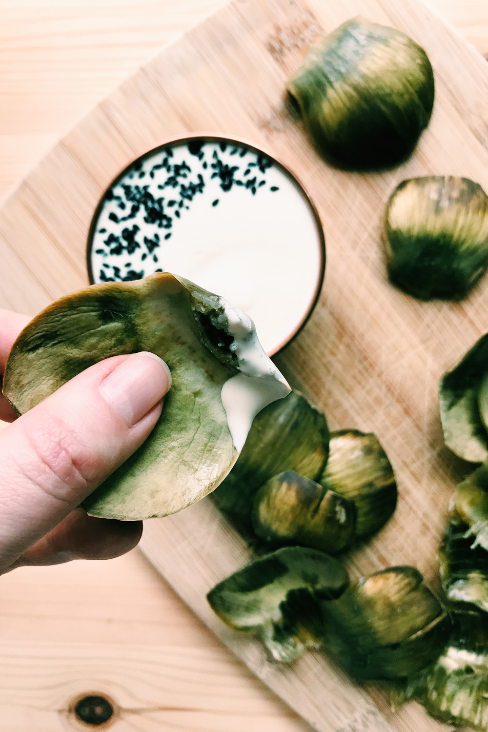 a hand holding an artichoke leaf with Kewpie mayo