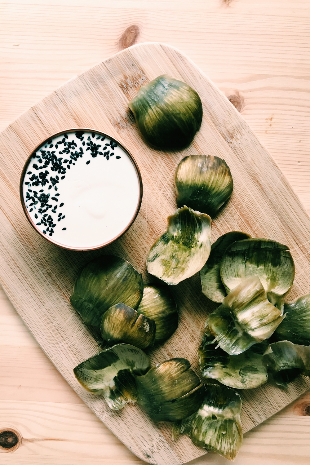 a copper bowl of Kewpie mayo and artichoke leaves on a wooden board