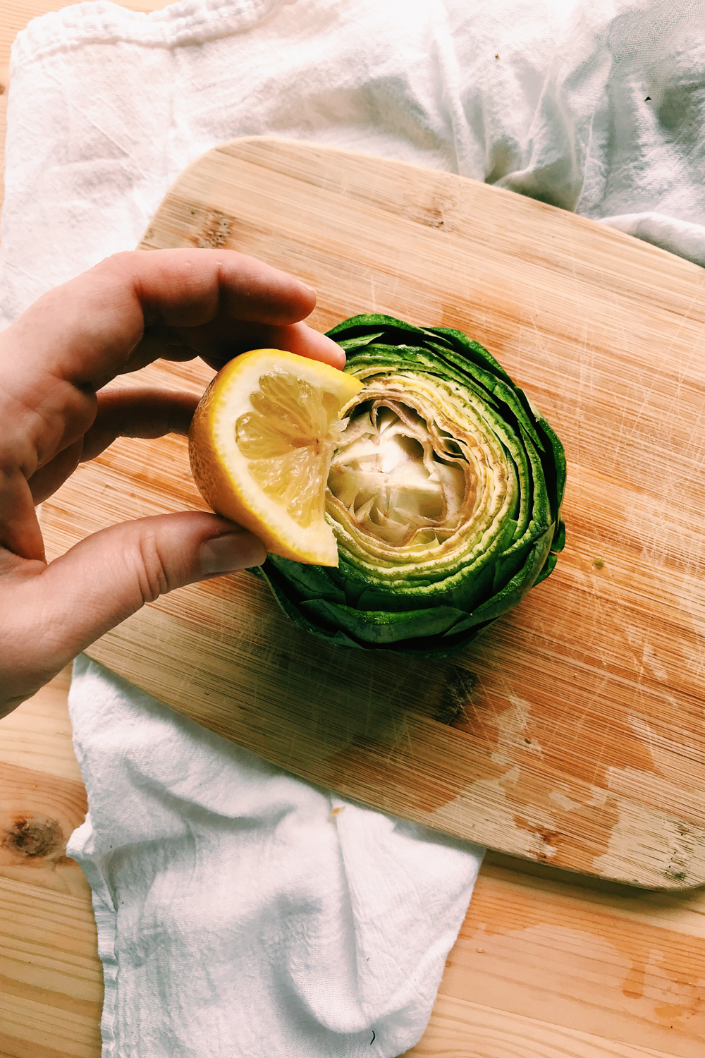 a hand squeezing lemon over a raw artichoke