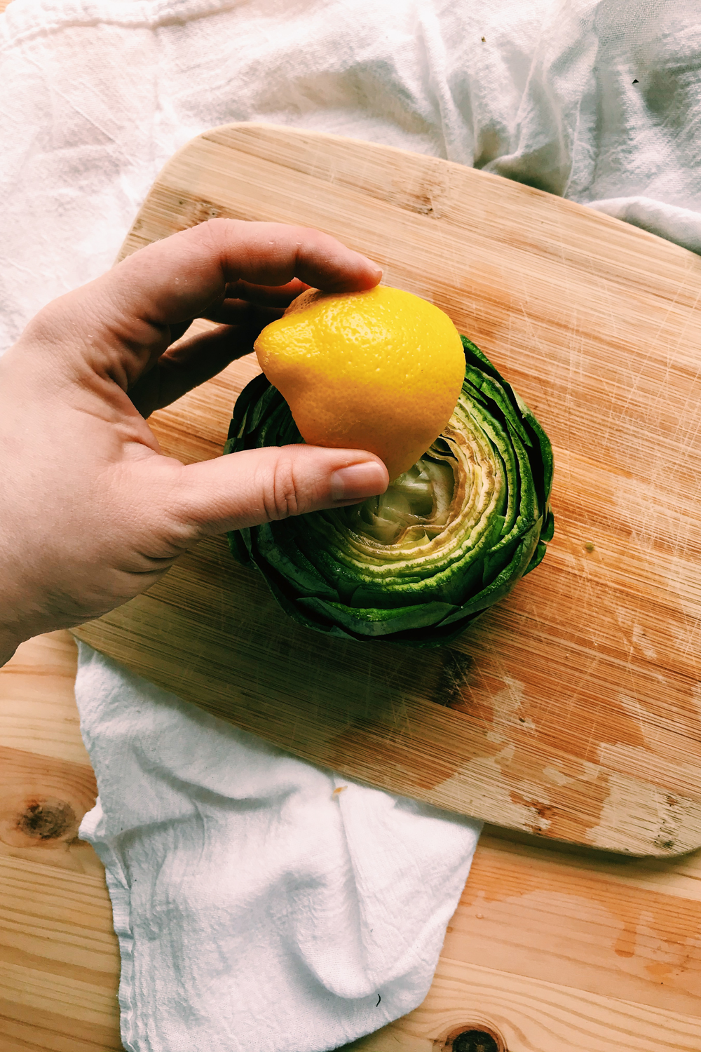a hand rubbing a raw artichoke with lemon