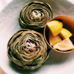 instant pot artichokes in a white dish with wedges of lemons in a copper bowl