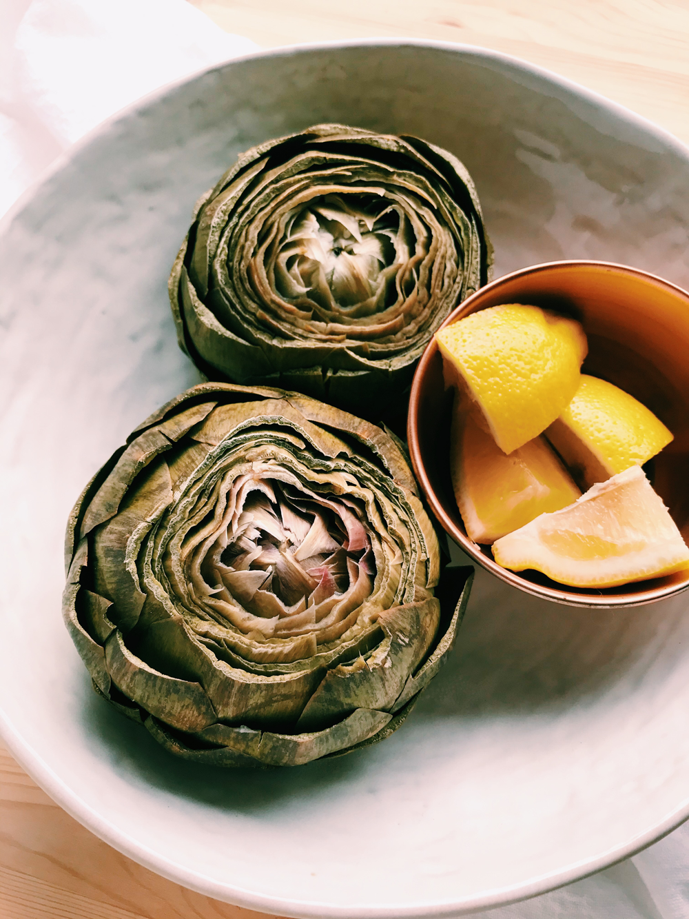 instant pot artichokes in a white dish with wedges of lemons in a copper bowl