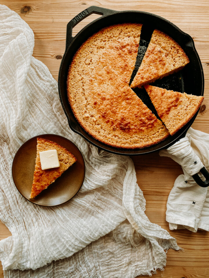 a cast iron skillet with corn bread next to a plate with a slice of cornbread and pat of butter