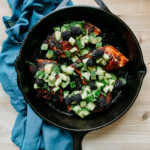 a cast iron pan resting on a blue towel with salmon and green salsa