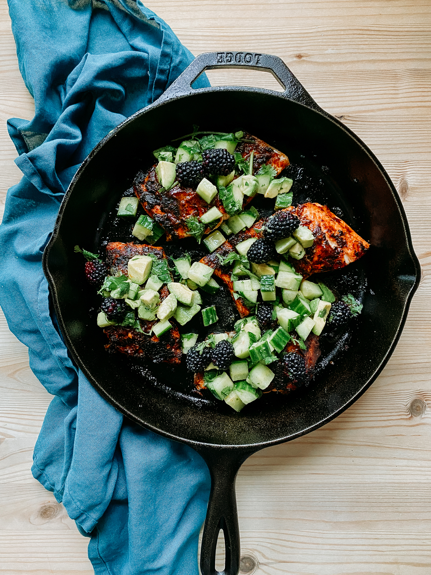 a cast iron pan resting on a blue towel with salmon and green salsa