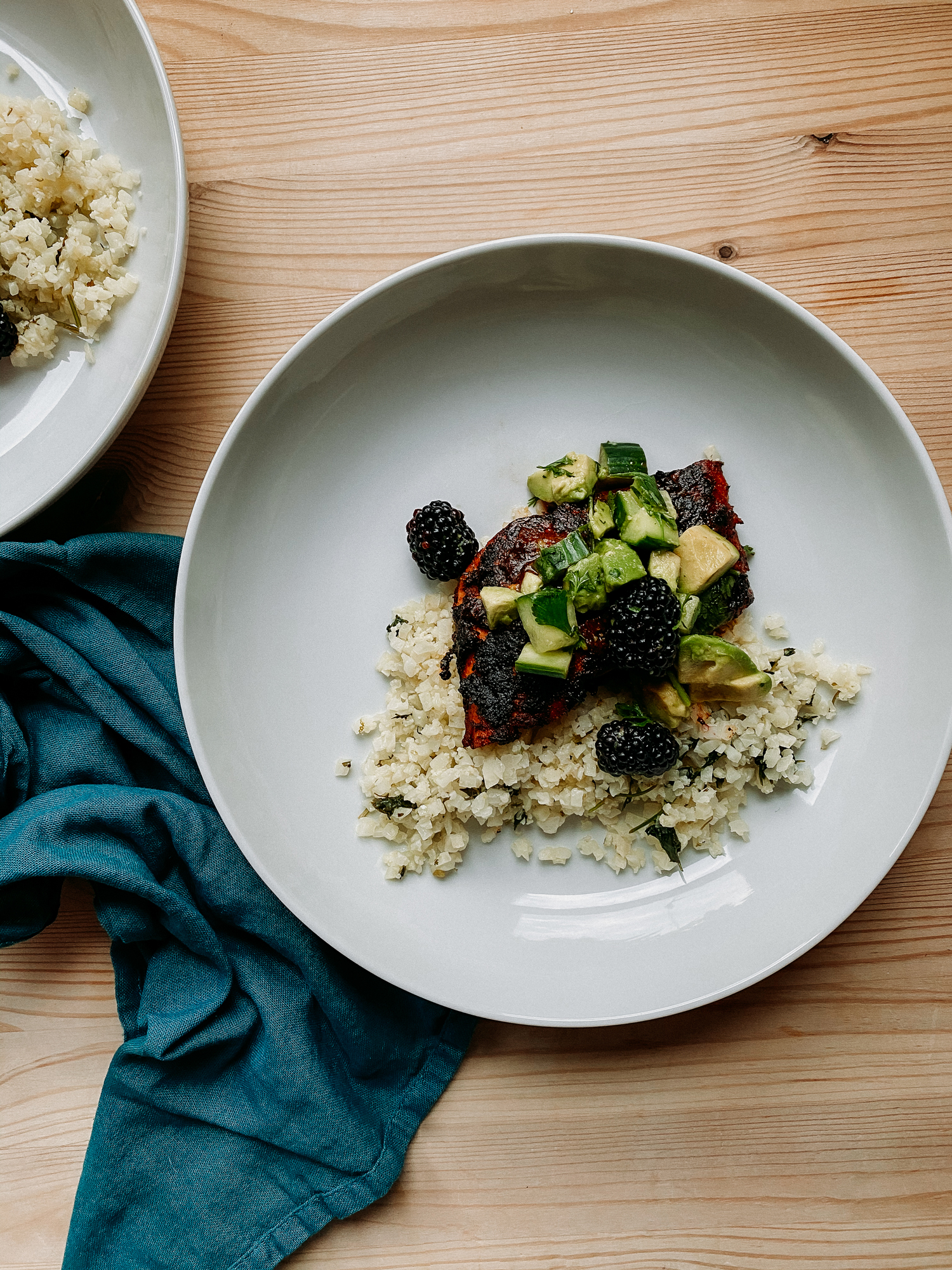 a white bowl containing cauliflower rice, cilantro, salmon with adobo sauce, and blackberry, cucumber, avocado salsa