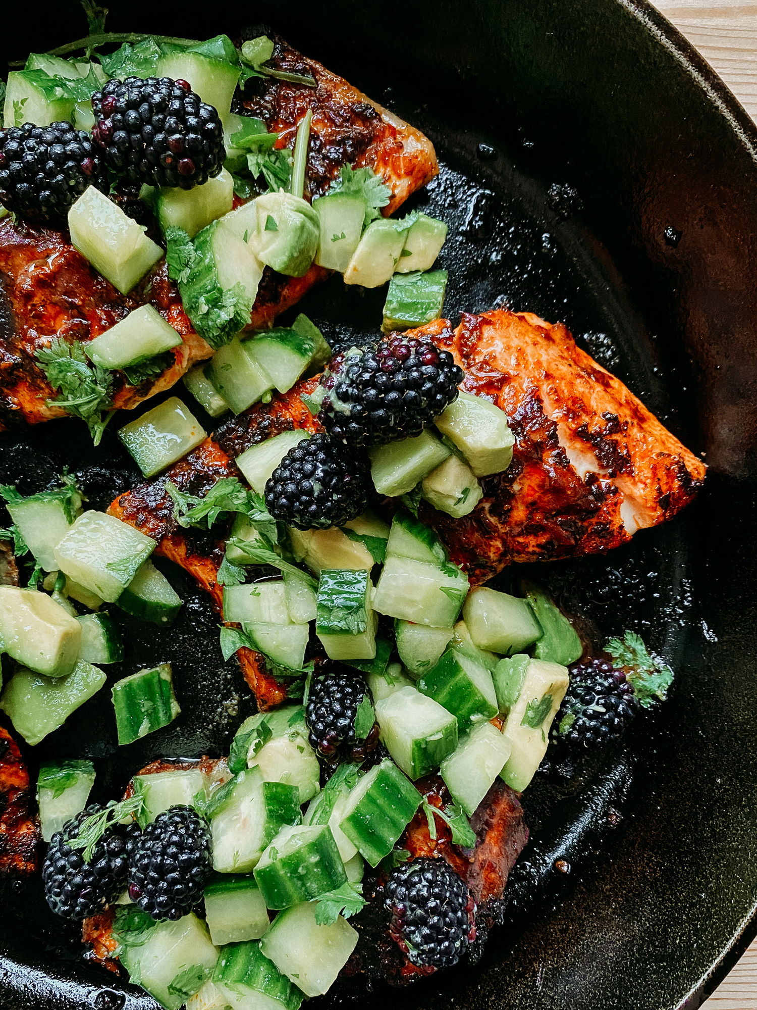 a closeup of a black cast iron pan with salmon with adobo sauce and blackberry cucumber avocado salsa on top