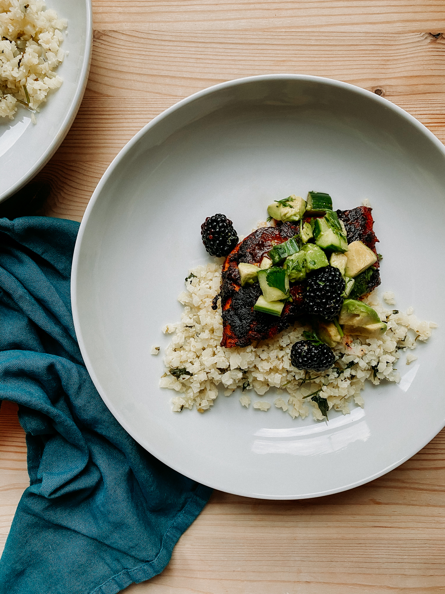 a white bowl with salmon with adobo sauce and cucumber, blackberry, and avocado salsa resting on top of a bed of cilantro lime cauliflower rice