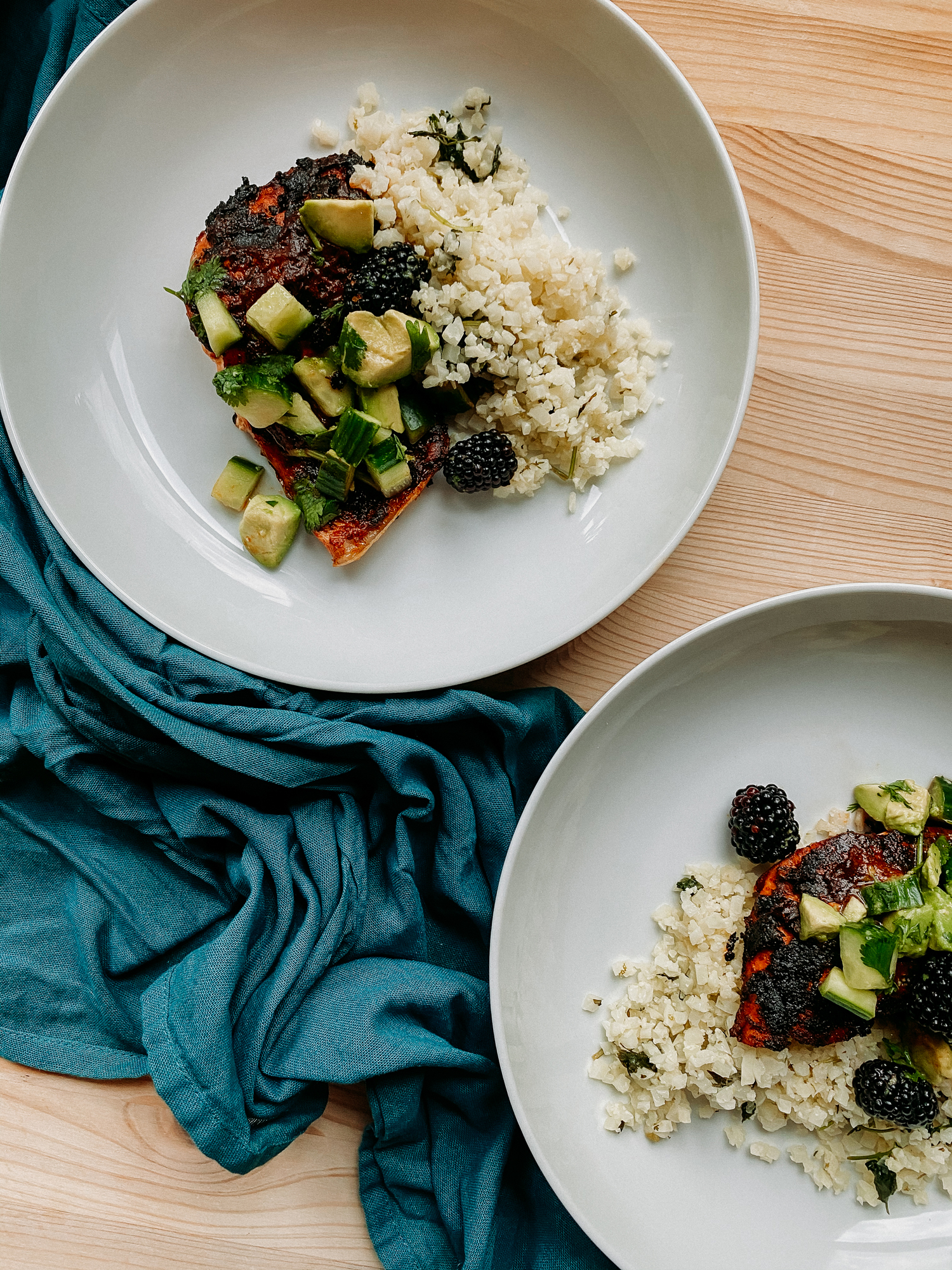 a blue towel with two white bowls that have spicy salmonw ith adobo sauce and a green salsa of blackberries, avocado, and cucumber inside