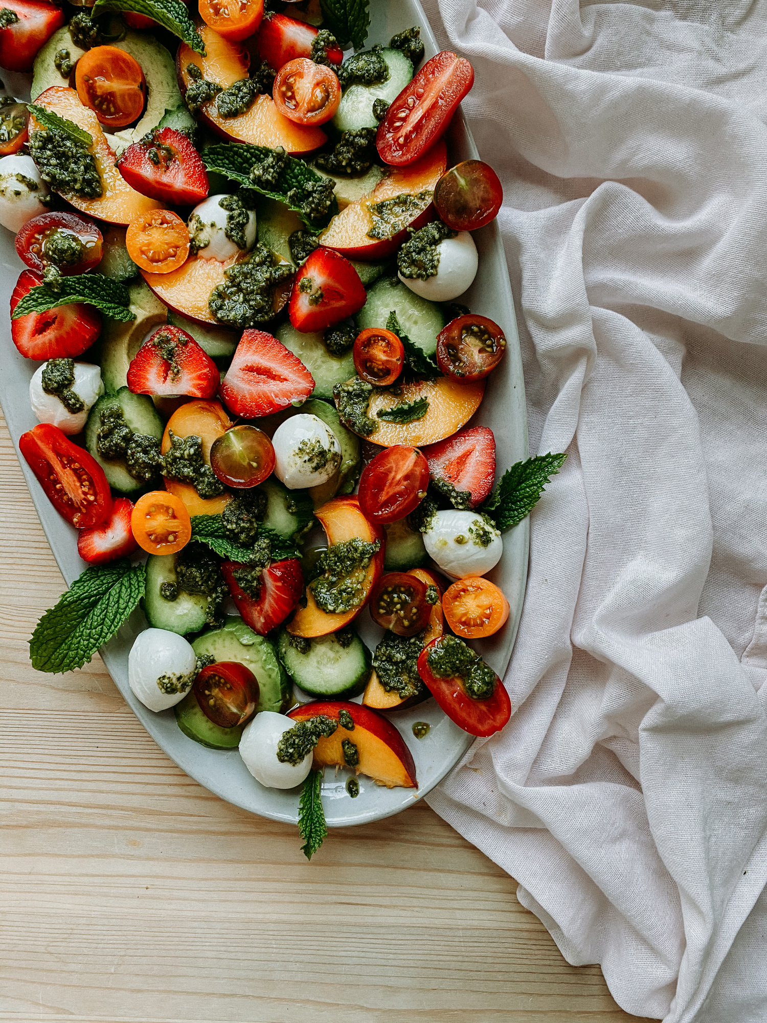 a white serving dish with a peach strawberry summer salad with basil walnut pesto
