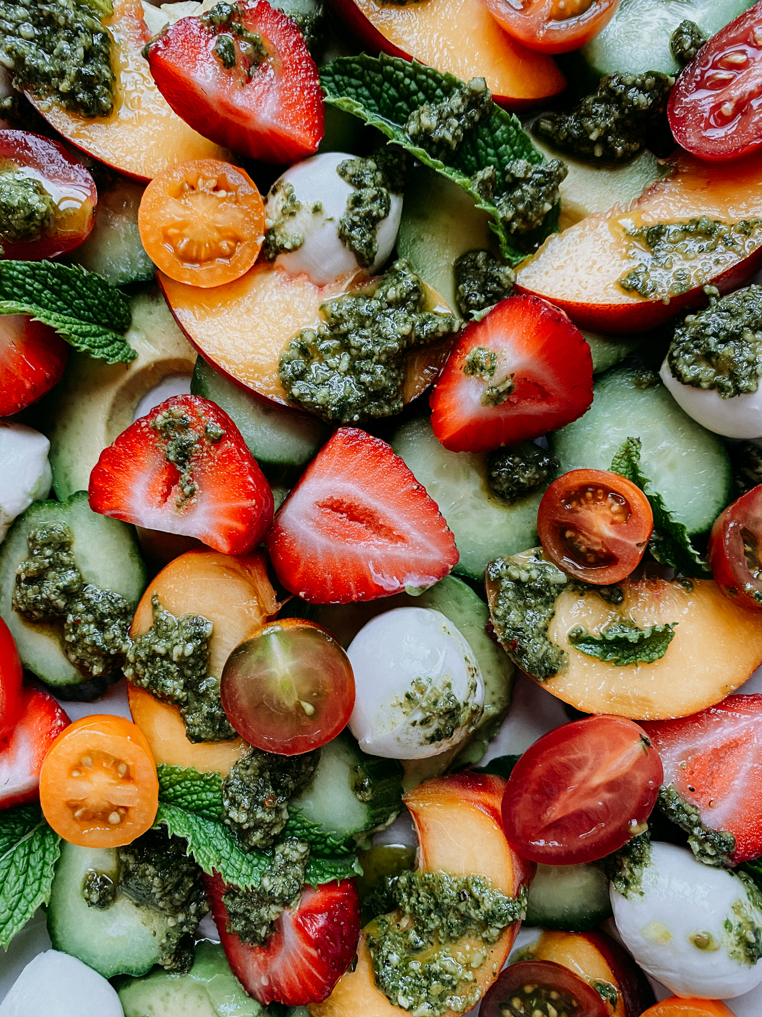 an assortment of strawberries, peaches, avocado, cucumber, pesto, tomato, and mozzarella