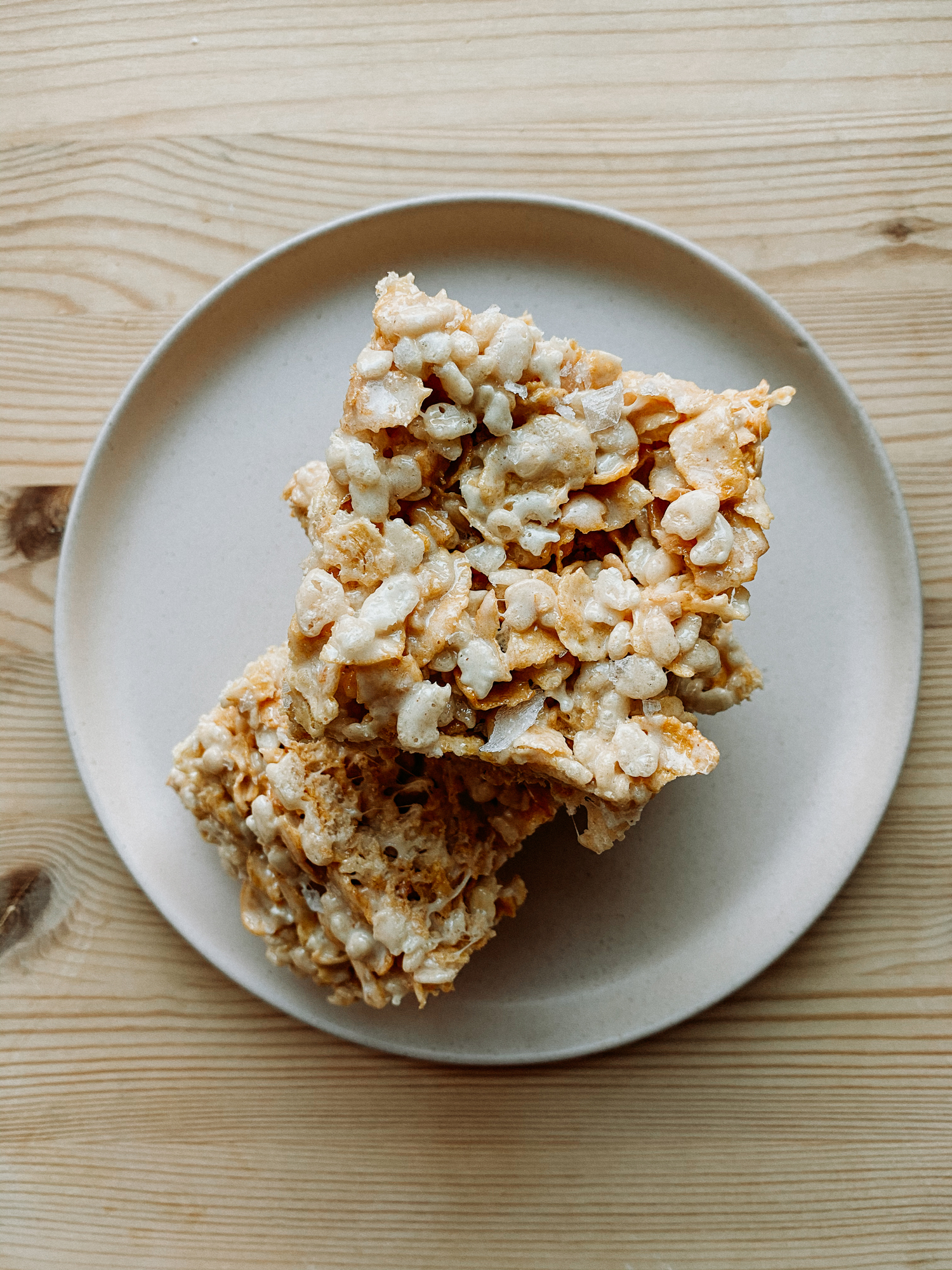 A stack of Salted Brown Butter Crispy Treats on a light pink plate resting on a wooden surface