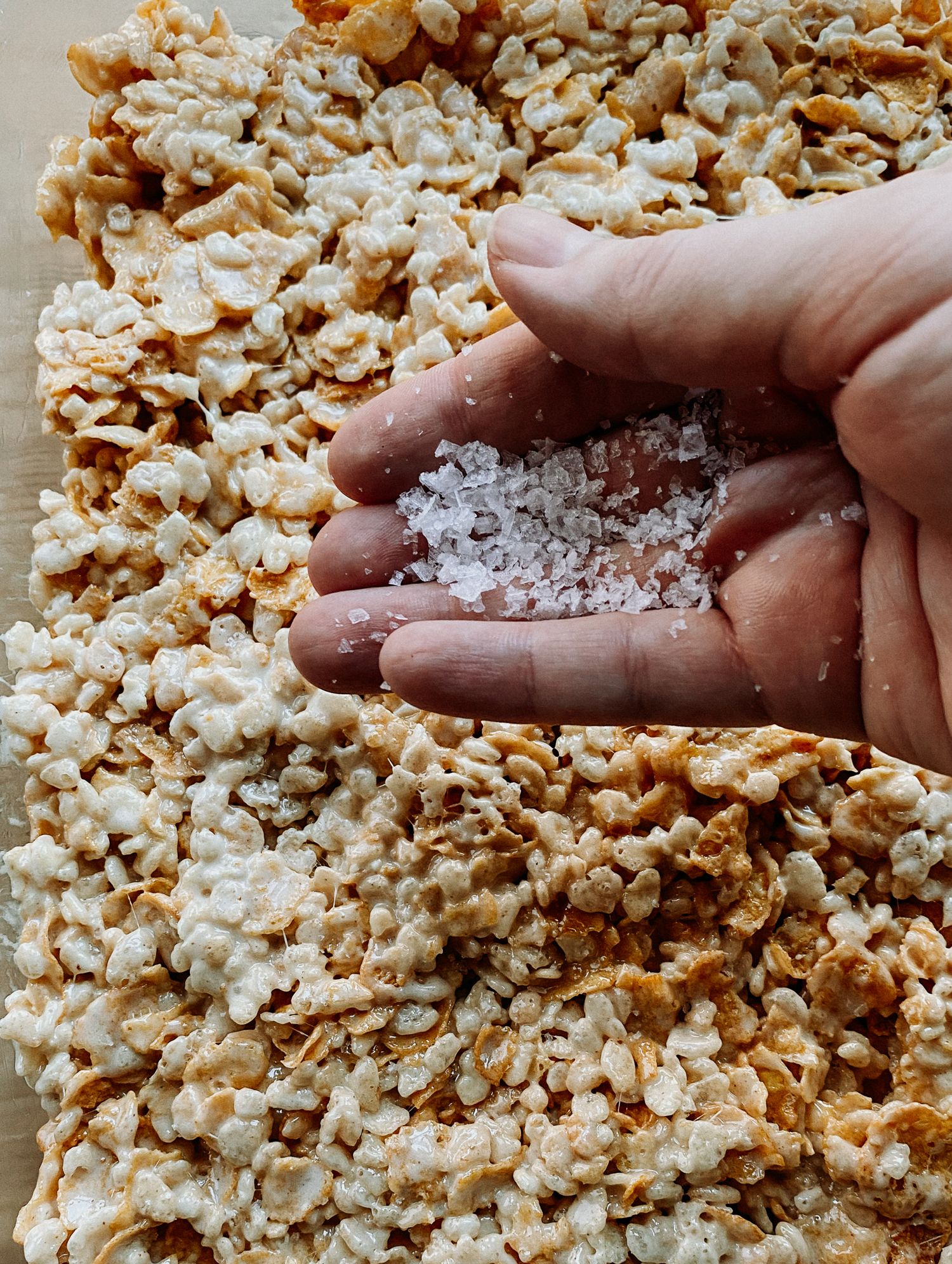a hand sprinkling flaked sea salt over the top of a tray of crispy treats