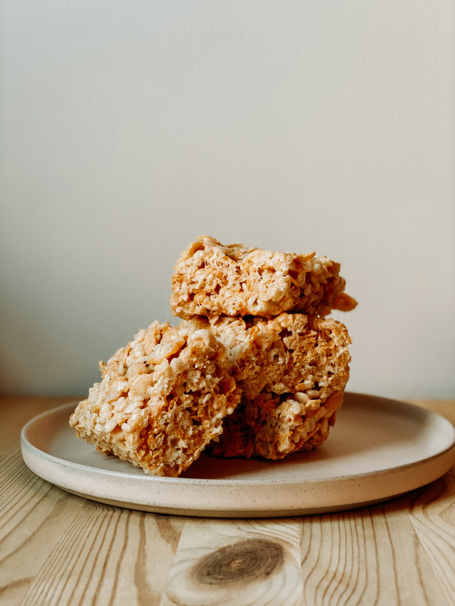 a square of Salted Brown Butter Crispy Treats resting on the side of a stack of the treat on a plate