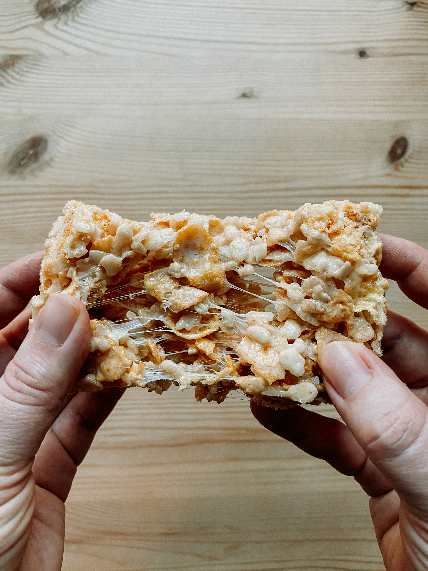 two hands pulling apart a Salted Brown Butter Crispy Treat over the top of a wooden surface