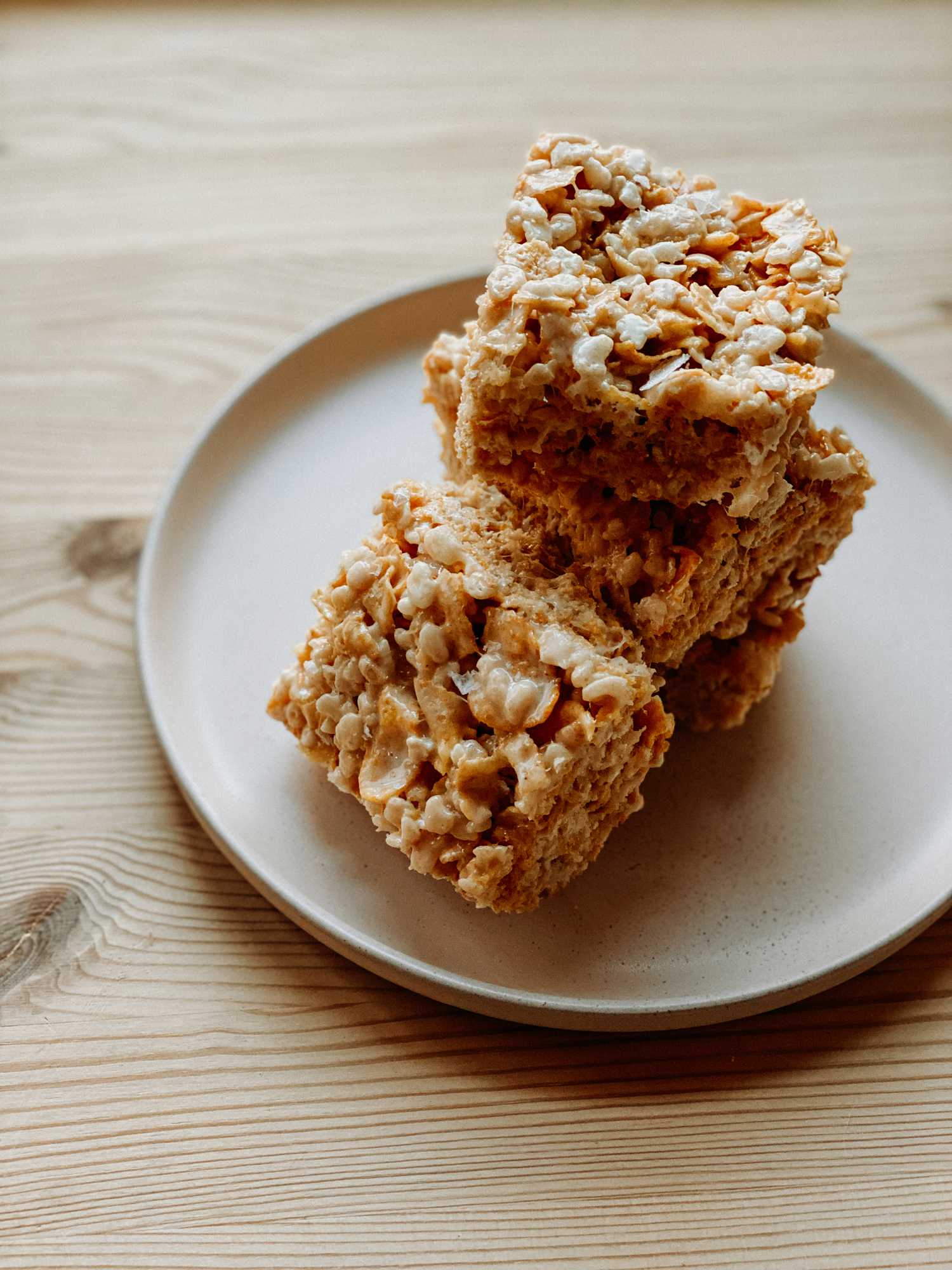 Salted Brown Butter Crispy Treats stacked on apink plate resting on a wooden table