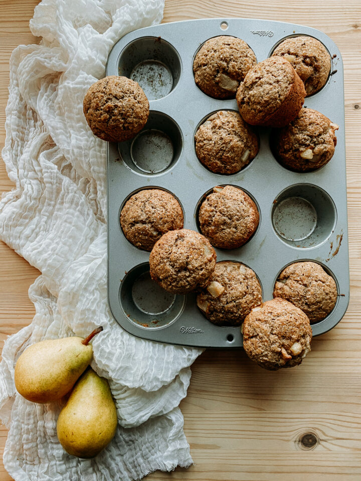 Sourdough Discard Spiced Pear Muffins in a baking tin setting on top of a piece of cheesecloth next to two fresh pears