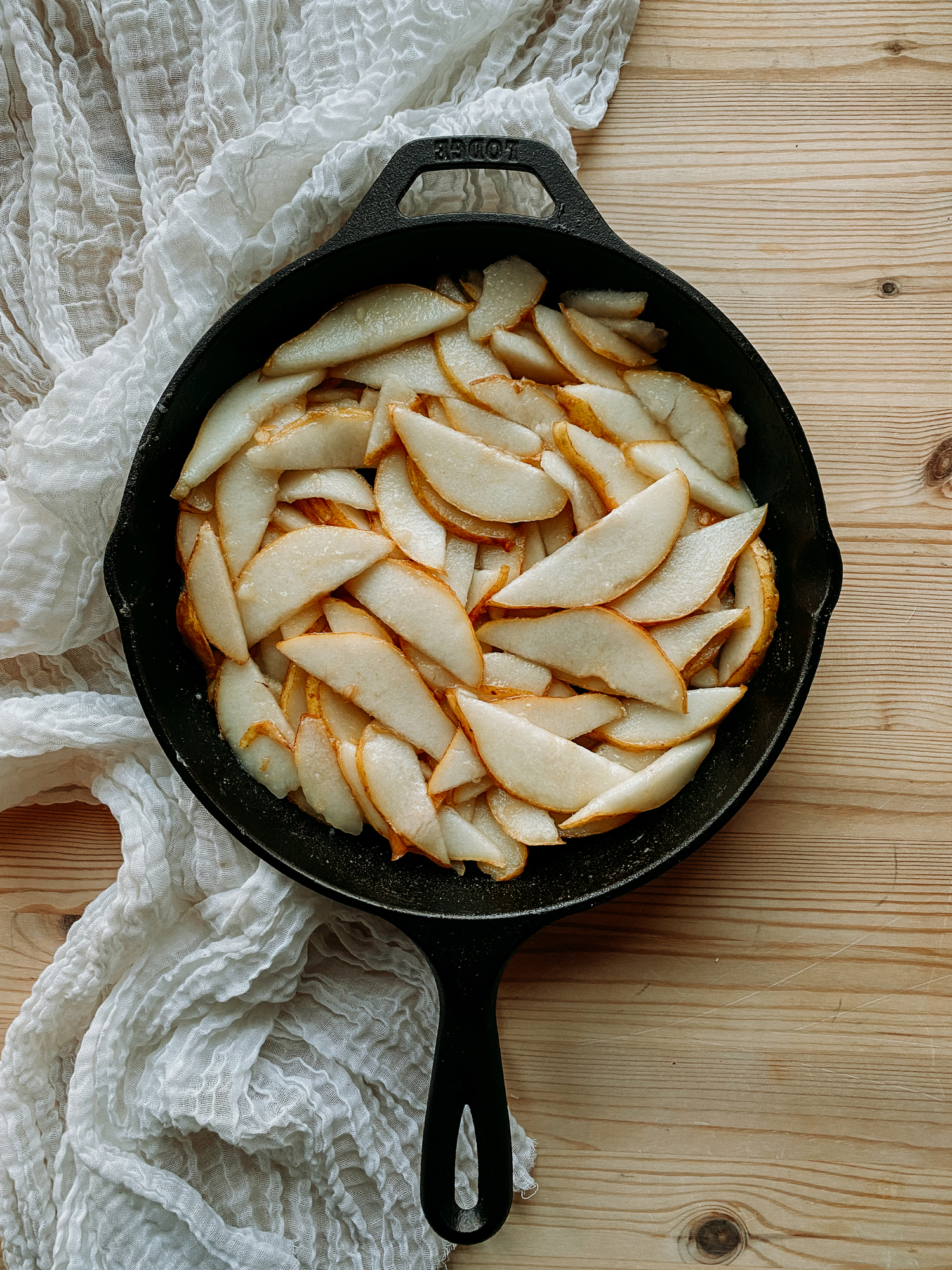 a cast iron pan filled with sliced pears resting on a cloth lined wooden surface