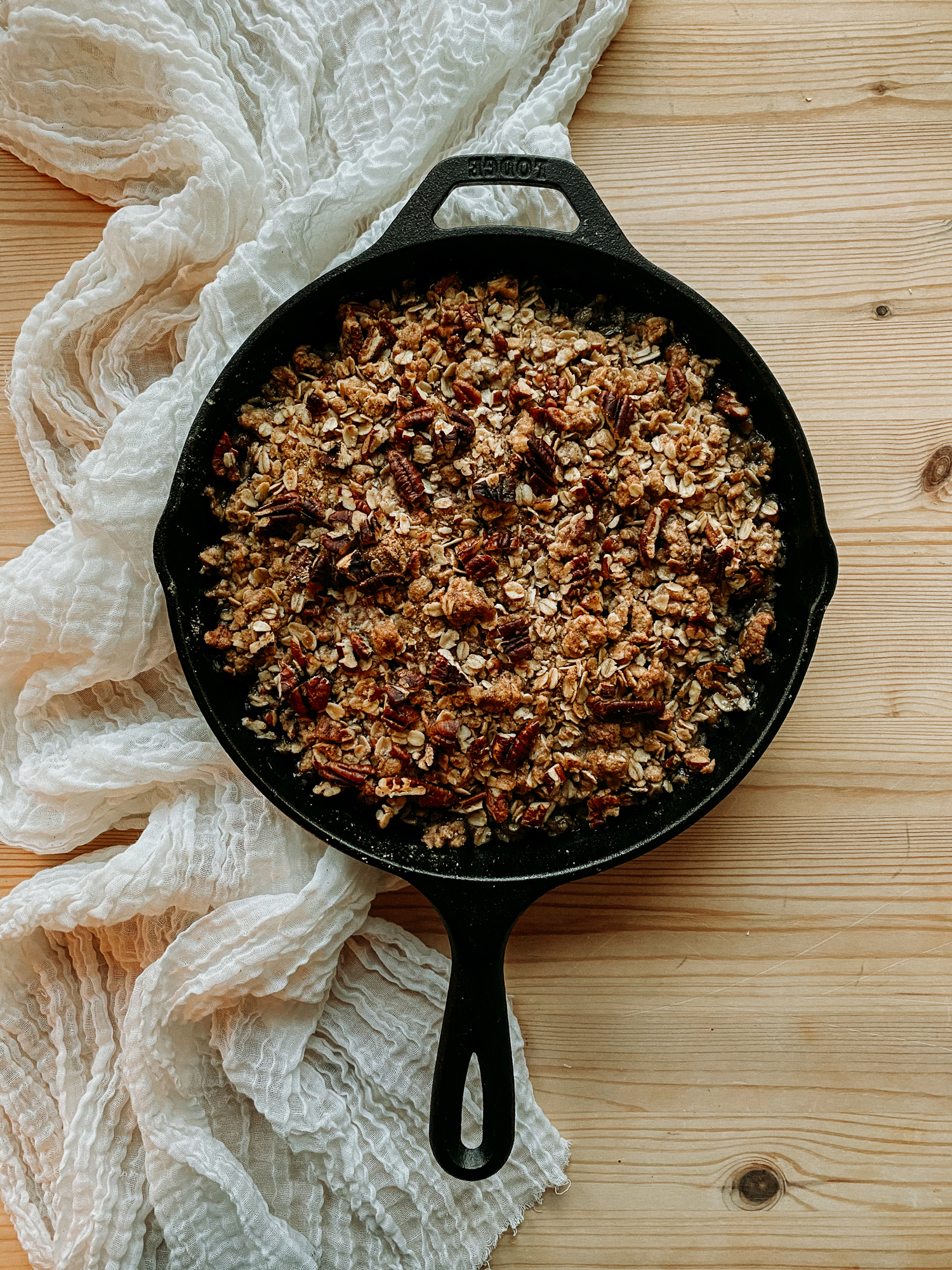 a cast iron pan with Spiced Pear Crisp resting on a piece of cheesecloth on a wooden table