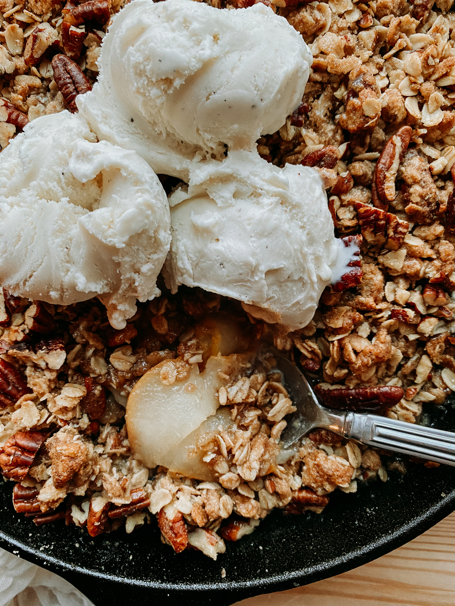 a closeup of a spoon resting in a pan of ice cream-topped Spiced Pear Crisp