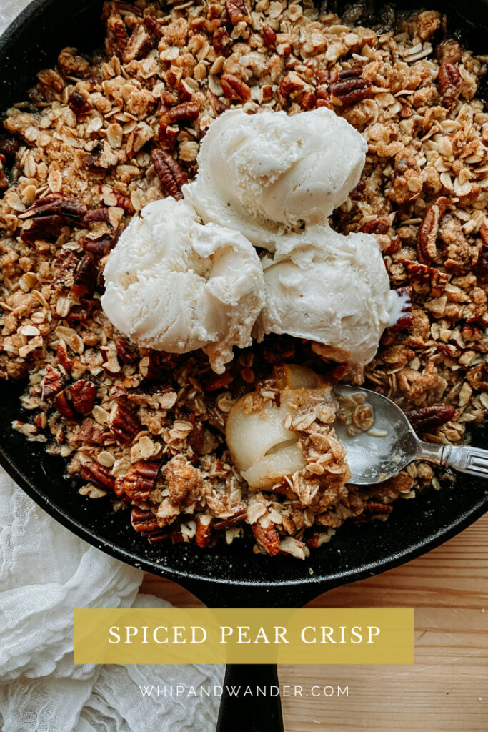 a closeup of a spoon dipping into a cast iron pan of crisp with pears and ice cream