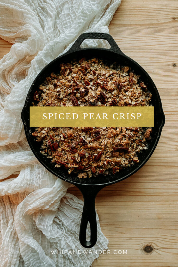 a cast iron pan of Spiced Pear Crisp resting on a cream colored fabric on a wooden surface