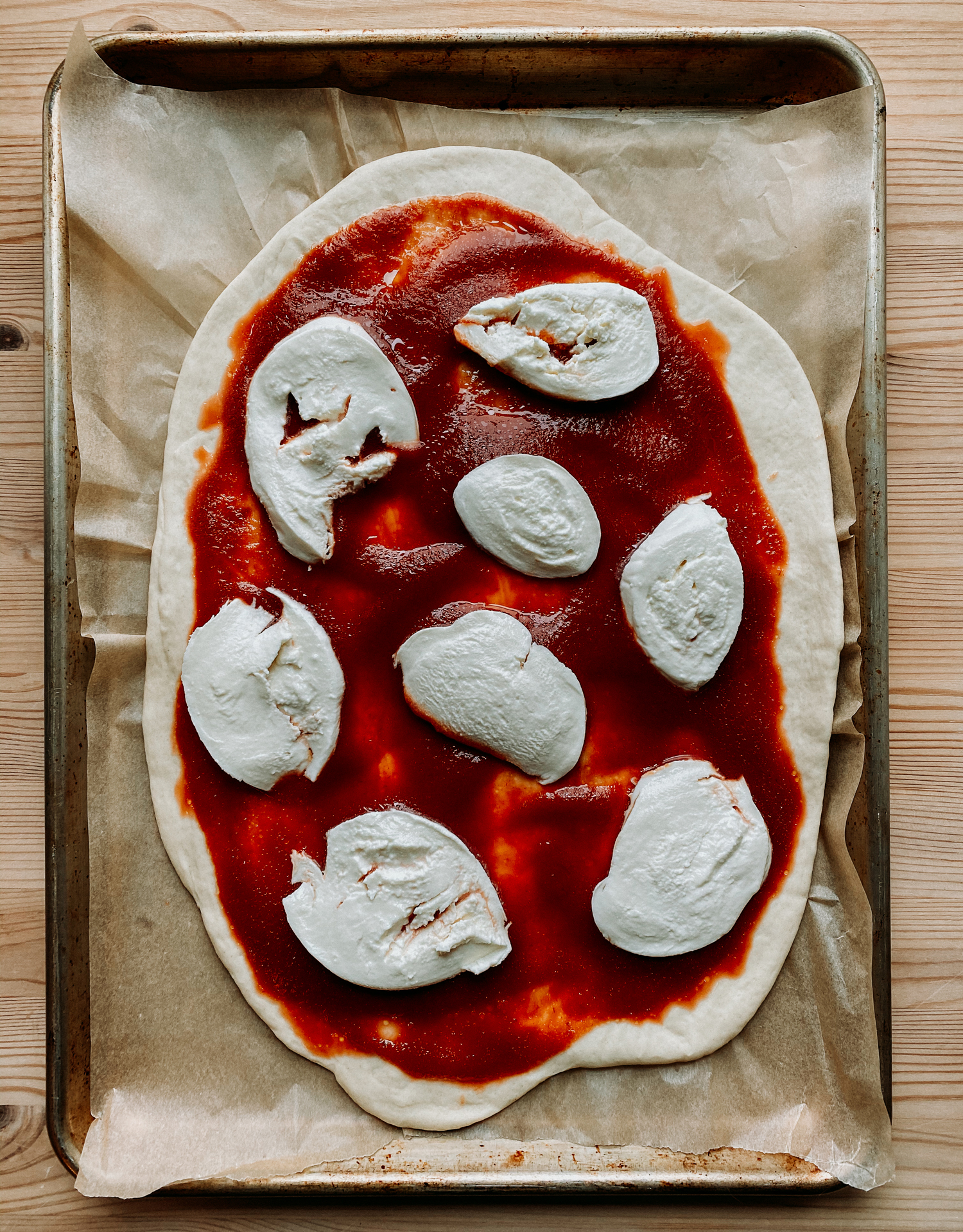 an unbaked pizza crust topped with tomato sauce and mozzarella resting on a baking tray