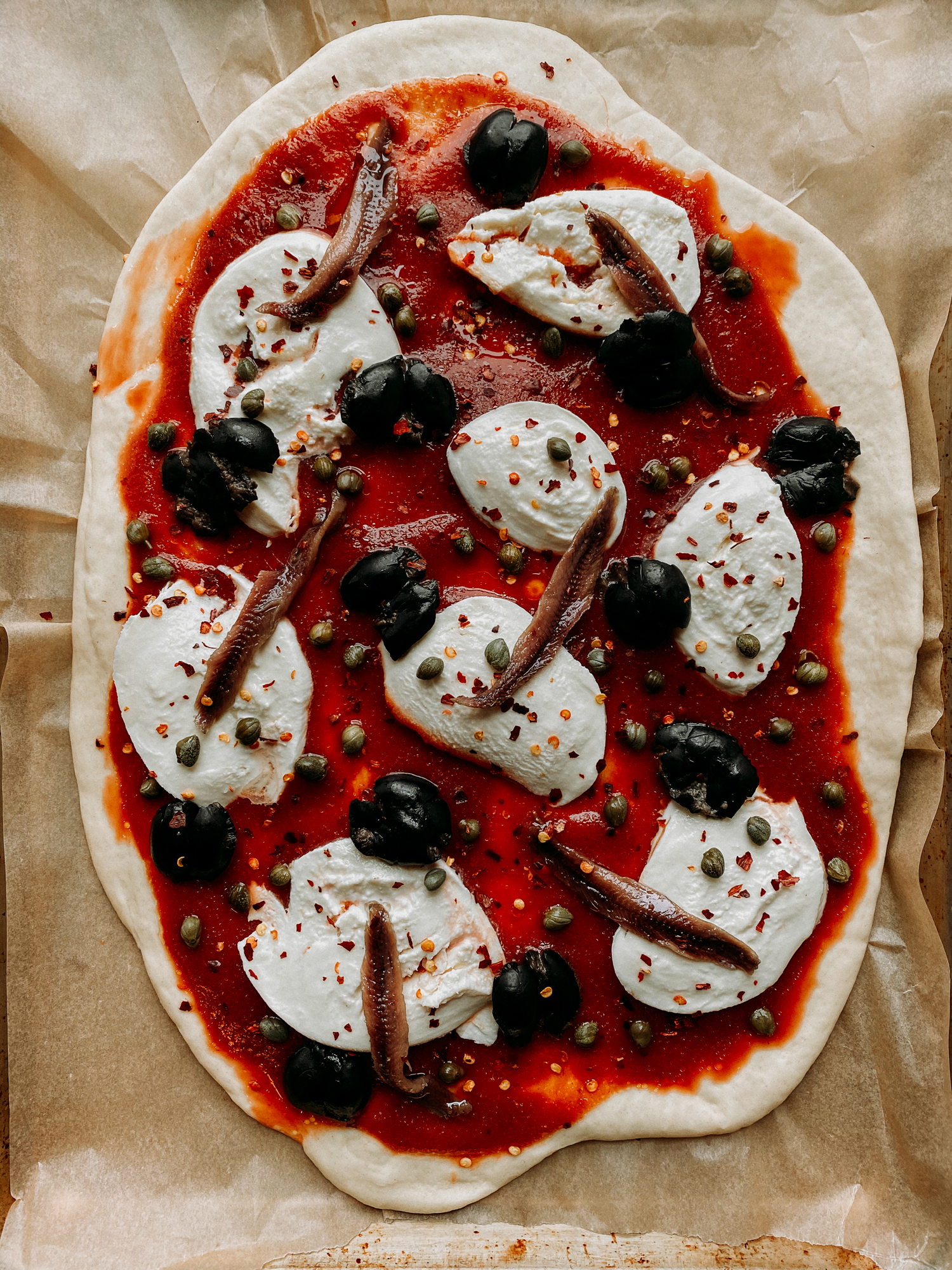 an unbaked Pizza Puttanesca resting on a baking tray