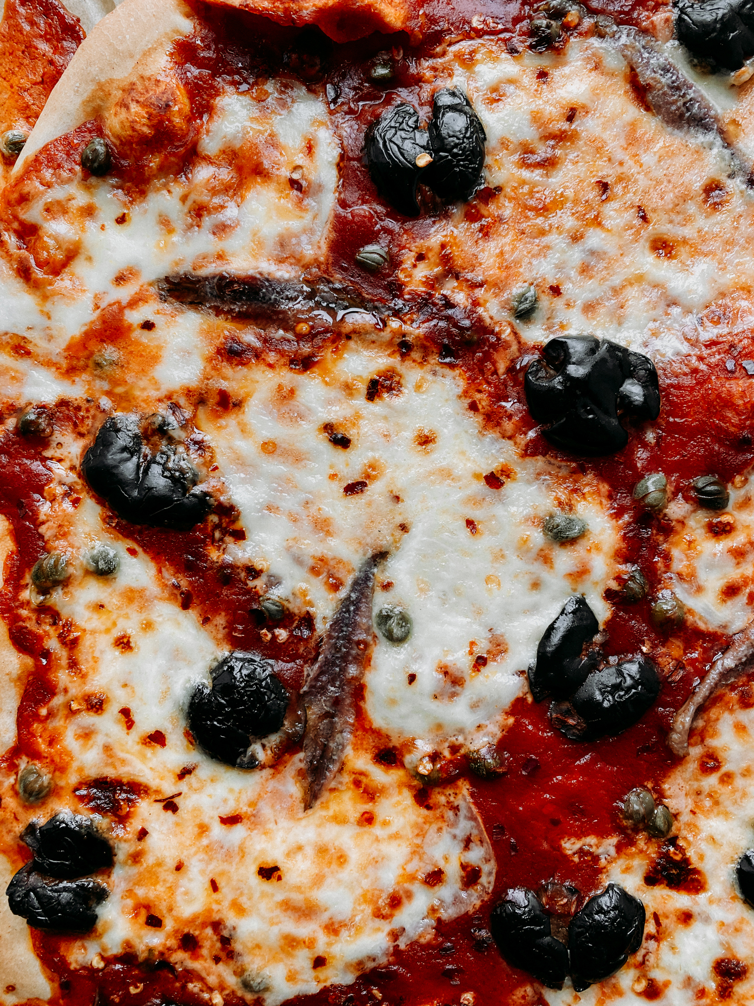 a closeup of browned mozzarella on top of a Pizza Puttanesca