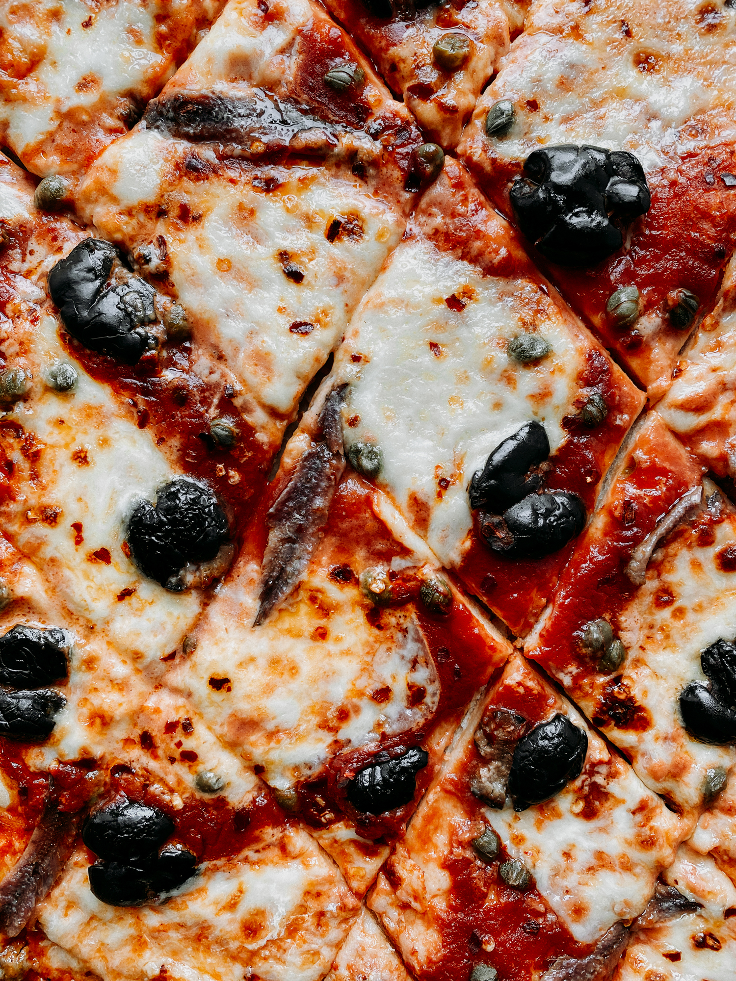 closeup of a Pizza Puttanesca that has been cut into diamonds