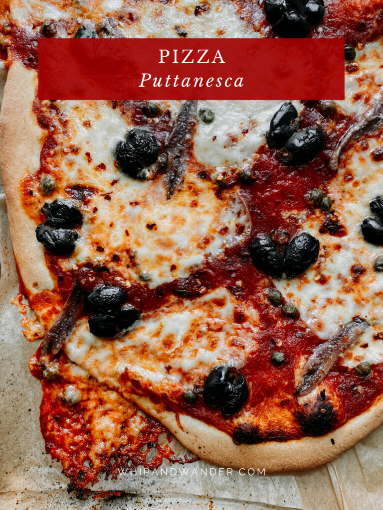a Pizza Puttanesca that has been pulled out of the oven and the cheese has melted over the edge and browned onto the baking sheet