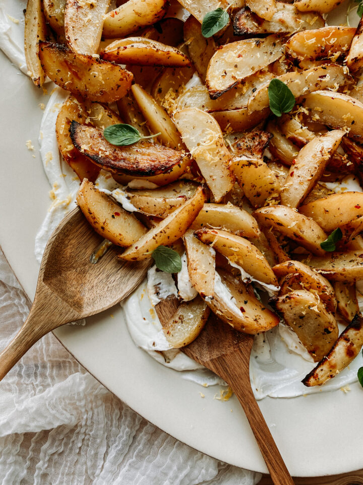 wooden serving utensils spooning Greek Potatoes and Whipped Feta from a large serving platter