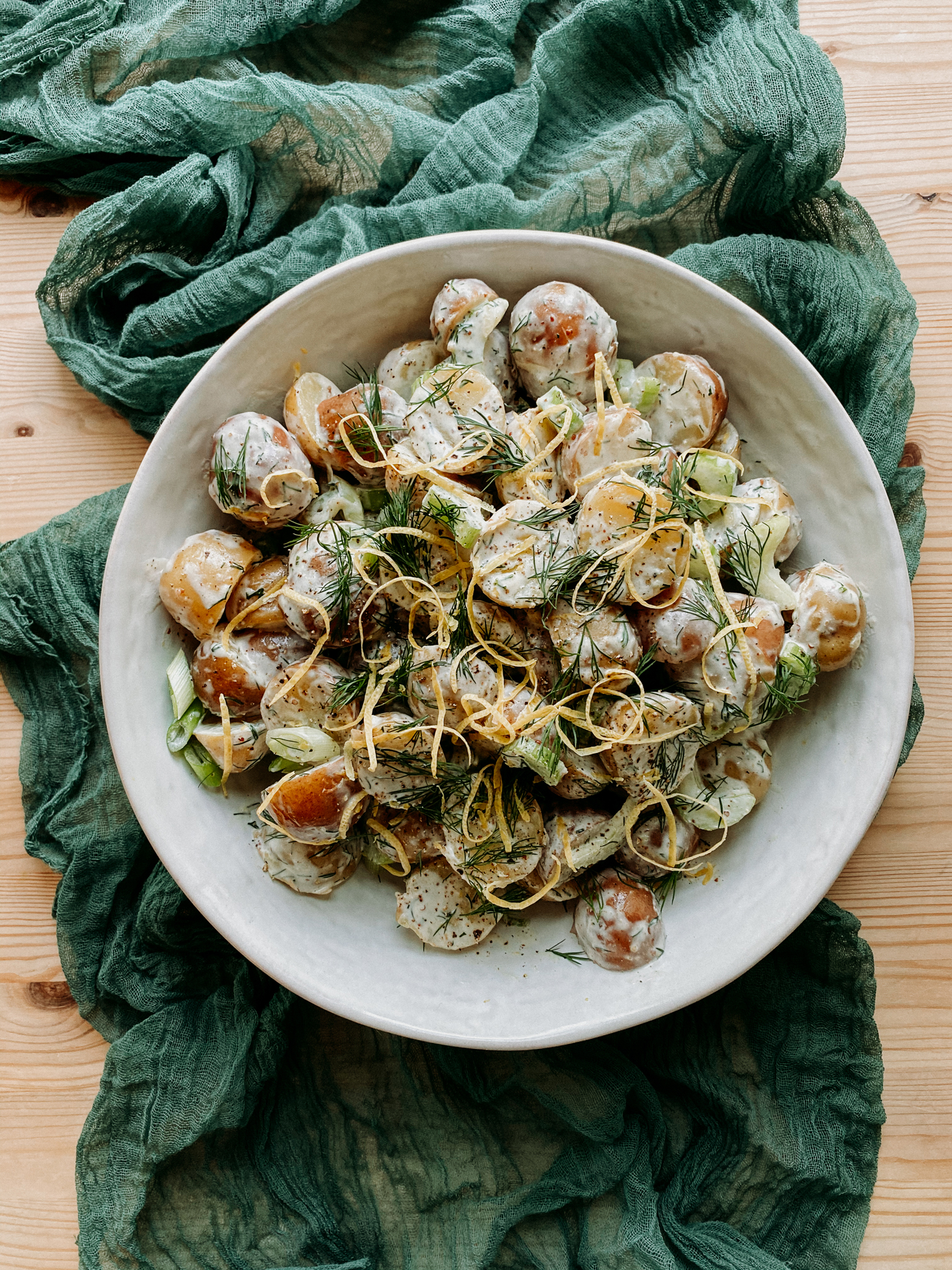 Creamy Dijon Dill Potato Salad in a white dish on top of a green cloth on a wooden table