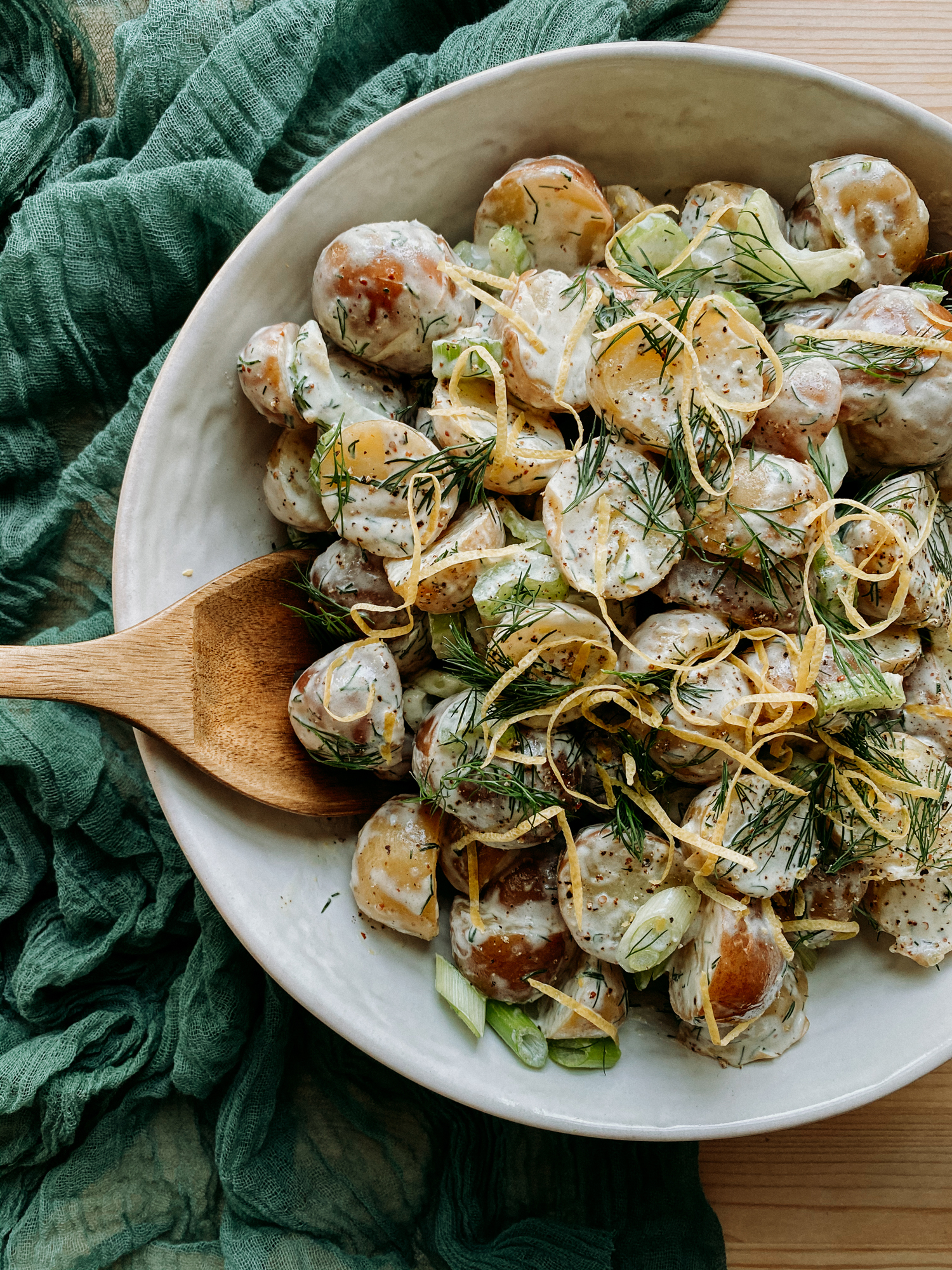 Creamy Dijon Dill Potato Salad in a white bowl with a wooden serving spoon resting in the bowl