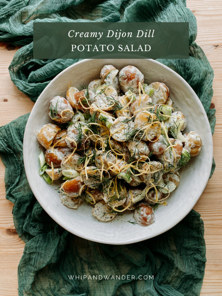 a large white bowl filled with potato salad resting on a green cloth on a wooden surface