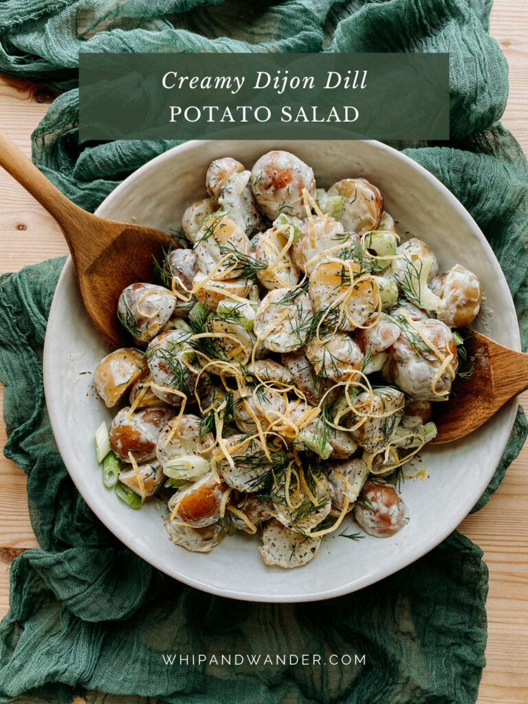 Creamy Dijon Dill Potato Salad in a white serving bowl with two wooden serving utensils resting in the bowl