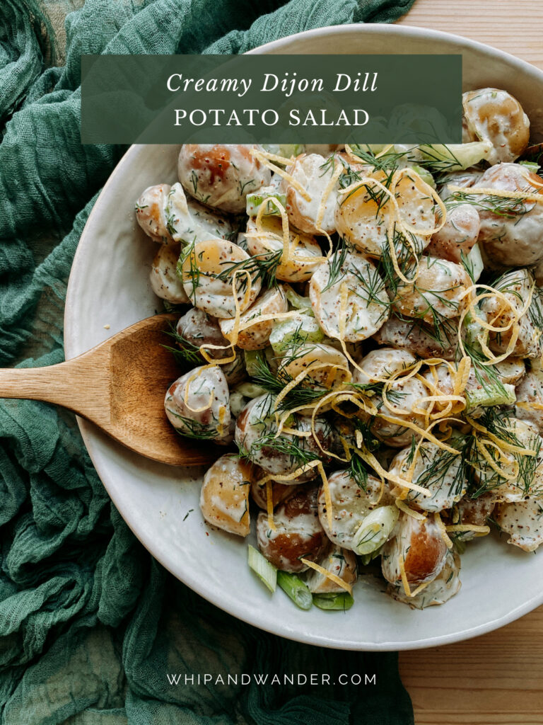 a wooden serving spoon dipping into a bowl of potato salad in a white bowl on a green cloth