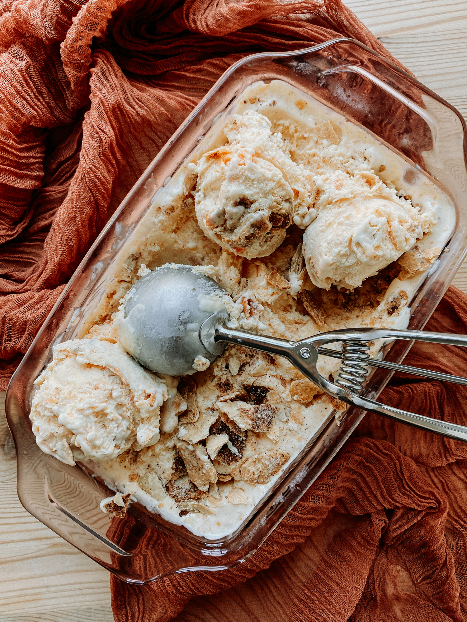 a metal ice cream scoop resting in a pan of Buttermilk Peach Pie Ice Cream