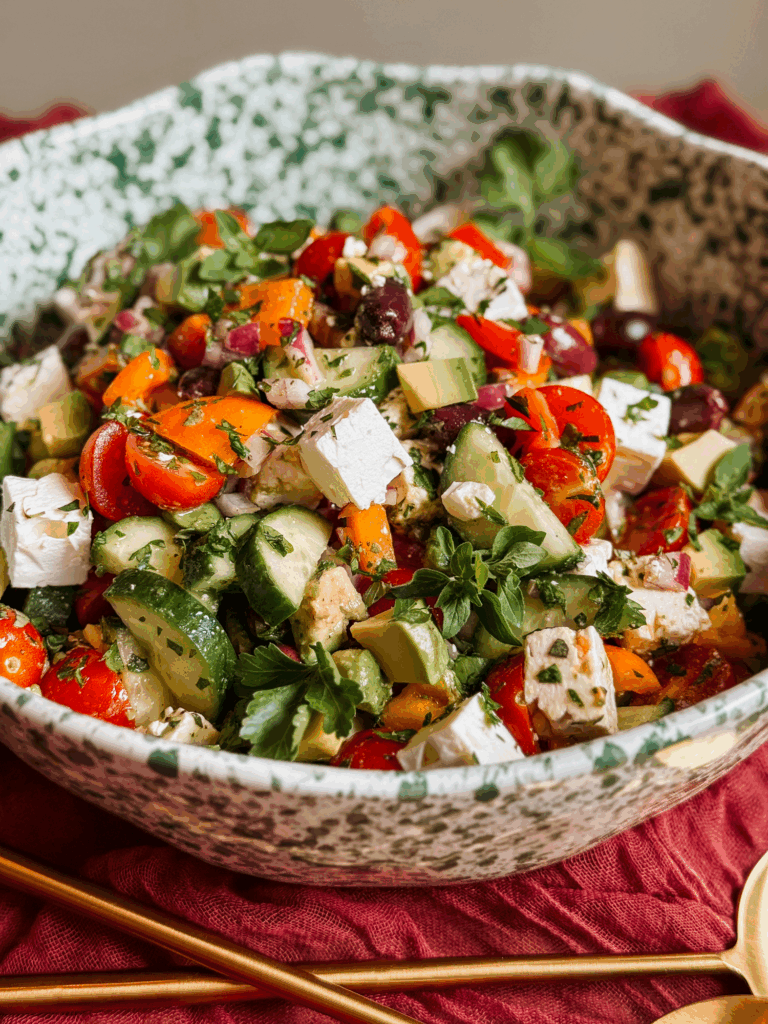 close-up of mediterranean greek salad with avocado, feta, cucumbers, olives, and tomatoes in a large serving bowl